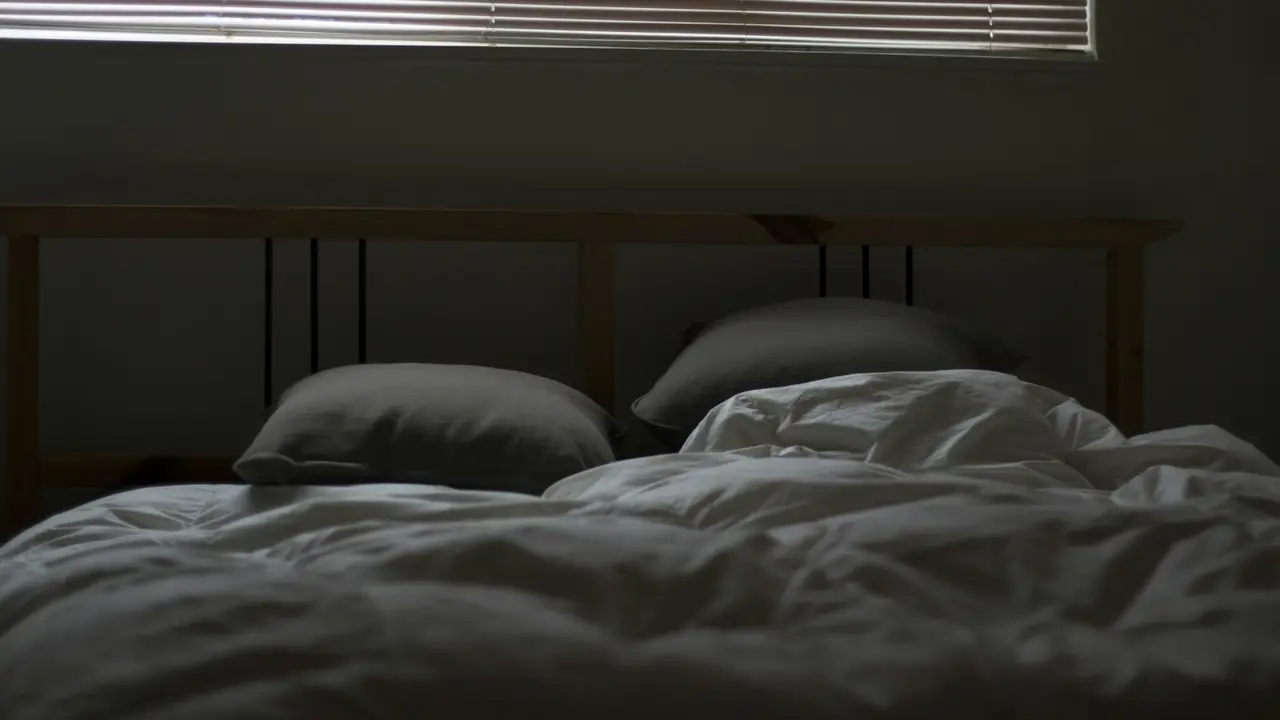 Slaapkamer in gedempt licht met een onopgemaakt bed