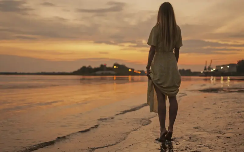 Vrouw die bij zonsondergang langs het strand loopt