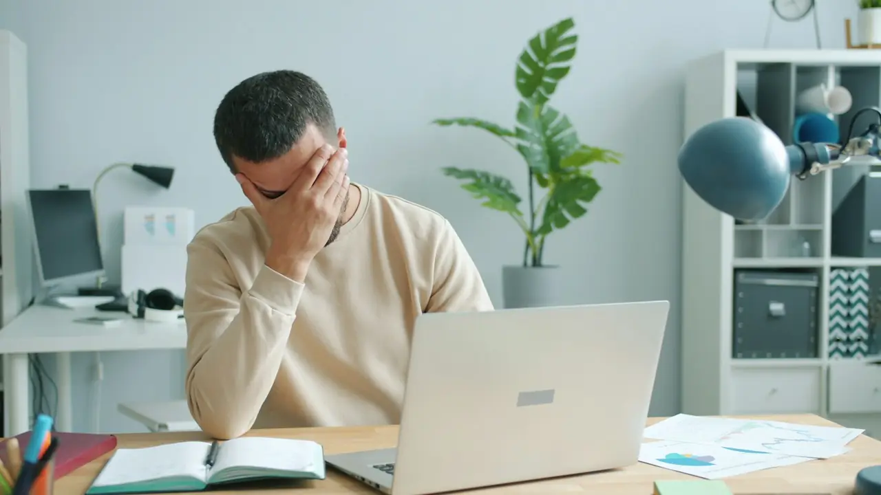 Man met zijn hand tegen zijn hoofd achter een laptop