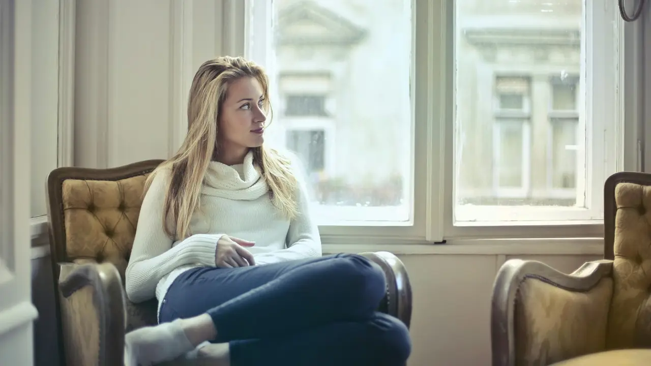 Vrouw zit in gedachten in een fauteuil bij het raam
